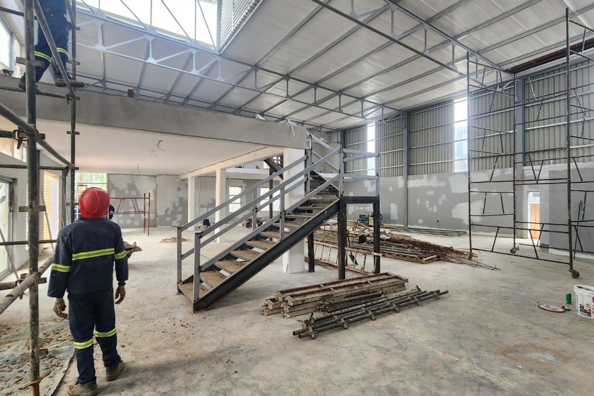 Spacious industrial warehouse interior currently under construction, featuring a mezzanine level, steel staircase, and high-volume exposed truss ceiling.