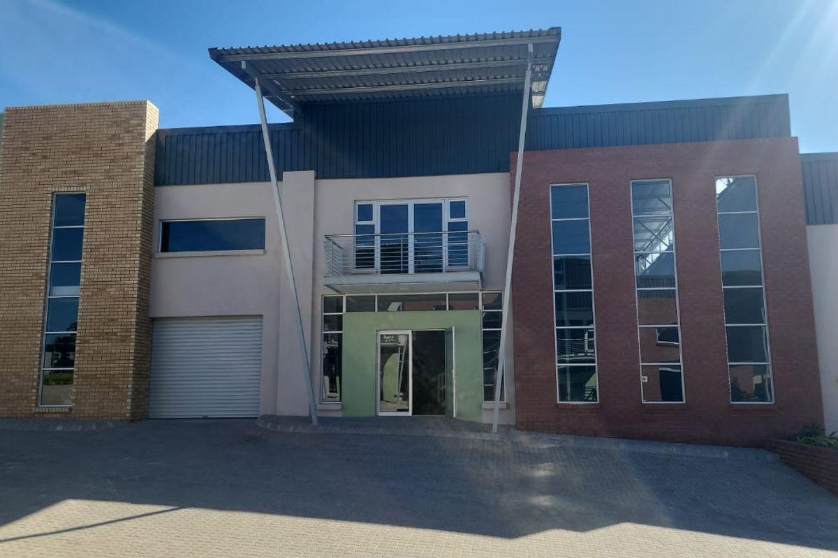 Modern industrial building facade featuring a combination of brick and plaster finishes, large glass windows, a roller shutter door, and a central balcony.