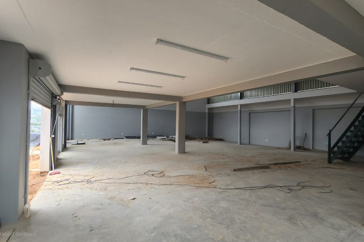 Spacious industrial open-plan warehouse area featuring high ceilings, structural support columns, a metal staircase, and a roller shutter door entrance.