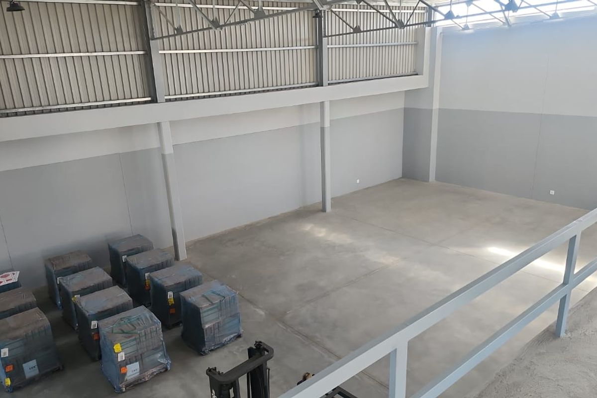 Spacious industrial warehouse unit featuring high ceilings, exposed steel roof trusses, concrete flooring, and a mezzanine level with safety railing.