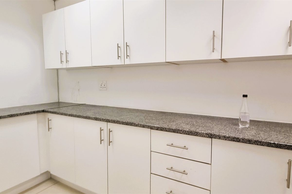 A clean office kitchenette featuring white cabinetry, granite countertops, and ample storage space.