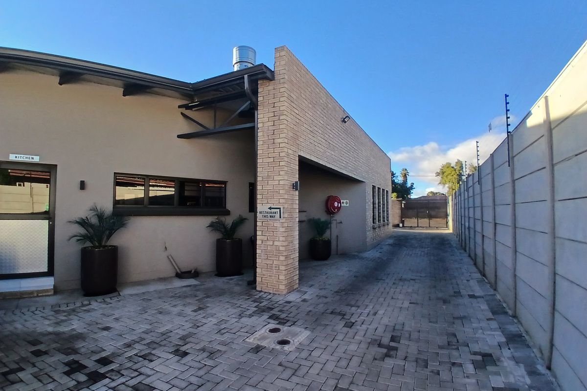 Exterior view of the guest house rear area featuring brick paving, a precast boundary wall with electric fencing, and access to the kitchen.