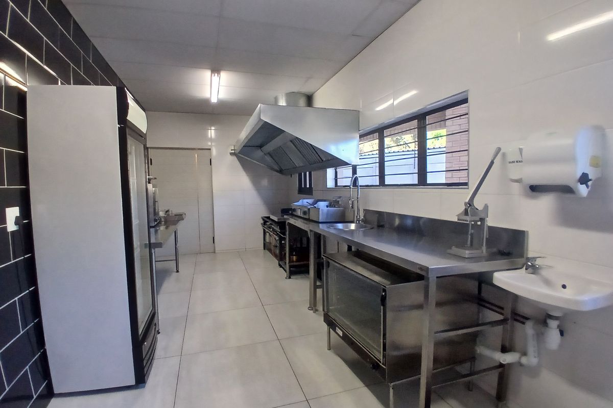 A clean, functional commercial kitchen featuring stainless steel prep surfaces, a professional extractor hood, commercial sink, and durable tiled finishes throughout.