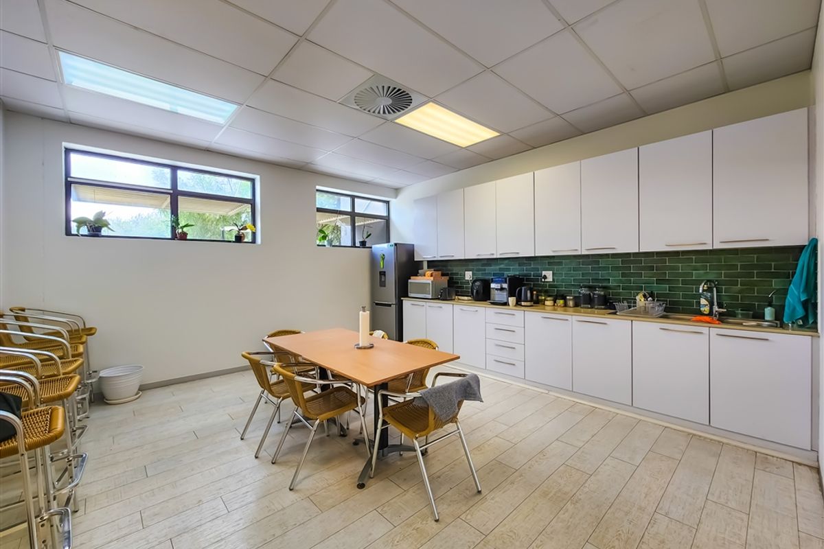 A functional office kitchenette featuring white cabinetry, a green subway tile backsplash, integrated sink, and wood-look tile flooring under a suspended ceiling.