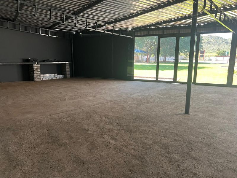 Spacious covered outdoor entertainment area featuring a built-in brick counter, exposed steel roof structure, and large glass sliding doors opening to the garden.