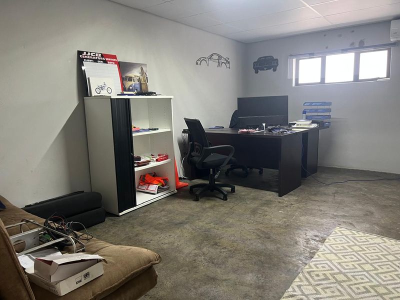 A functional office space featuring exposed concrete flooring, a suspended ceiling, and an integrated air conditioning unit.