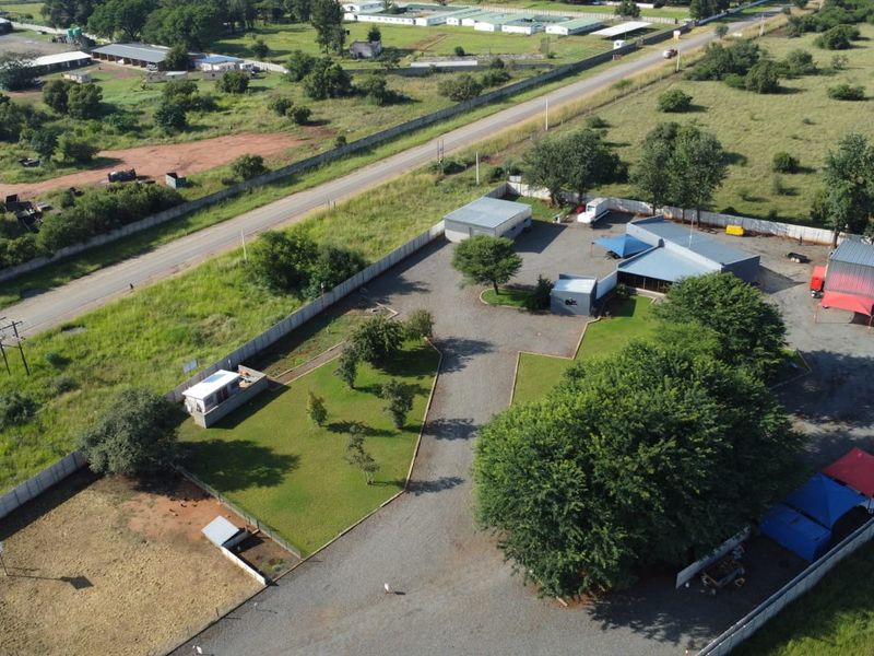 Aerial view of a commercial property featuring multiple outbuildings, gravel driveway, shade cloth parking areas, and fenced grounds.