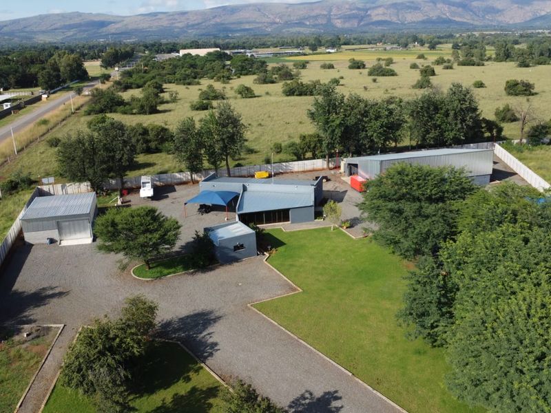 Aerial view of a commercial property featuring multiple metal-roofed structures, a gravel driveway, and expansive landscaped grounds in a rural setting.