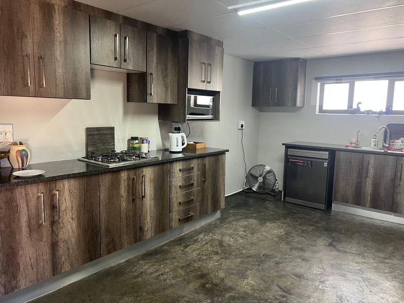 A functional kitchen featuring dark wood-grain cabinetry, granite countertops, a built-in gas hob, and a stainless steel sink with a modern mixer tap.