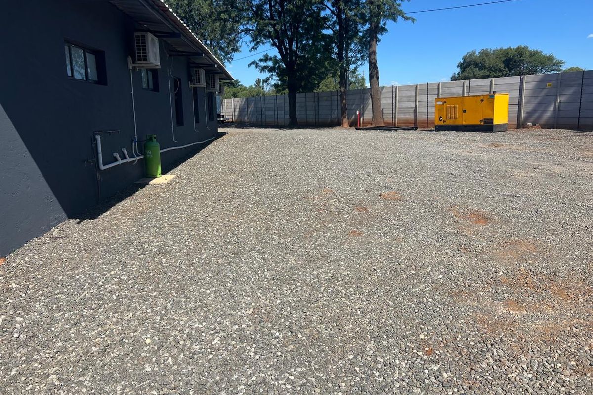 A spacious gravel-surfaced rear yard area featuring a perimeter precast concrete wall, external air conditioning units, and a dedicated backup generator.
