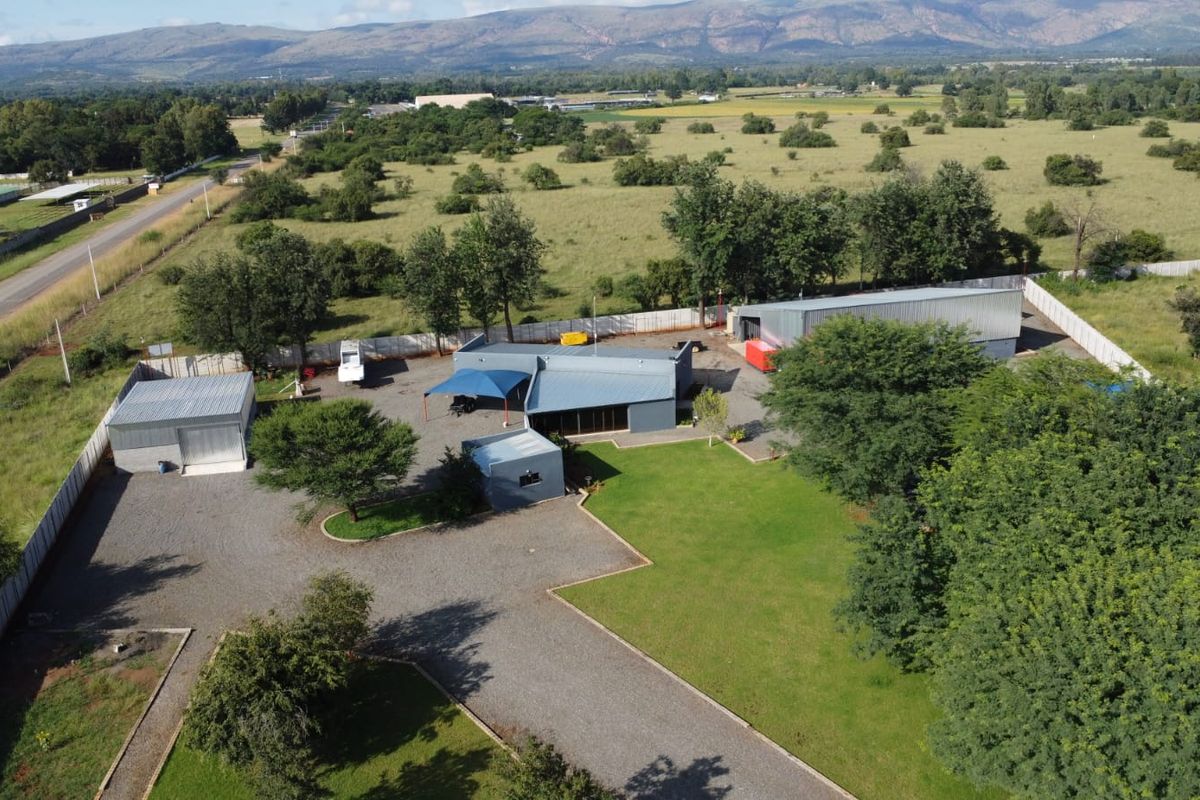Aerial view of a commercial property featuring multiple metal-roofed structures, a gravel driveway, and expansive landscaped grounds in a rural setting.