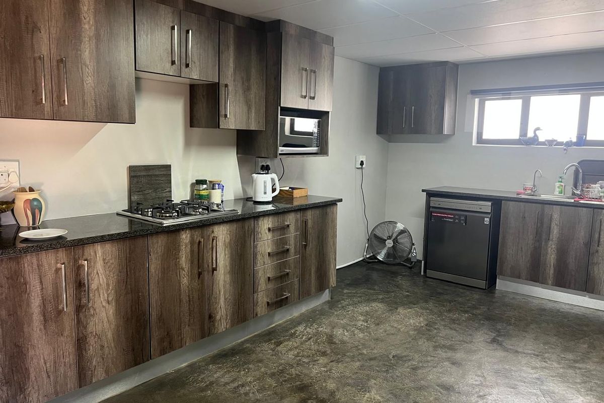 A functional kitchen featuring dark wood-grain cabinetry, granite countertops, a built-in gas hob, and a stainless steel sink with a modern mixer tap.