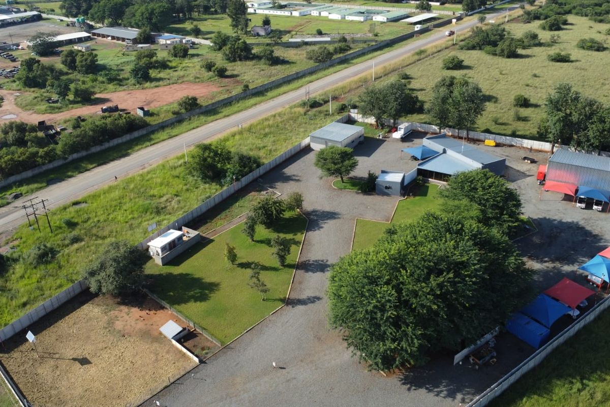 Aerial view of a commercial property featuring multiple outbuildings, gravel driveway, shade cloth parking areas, and fenced grounds.
