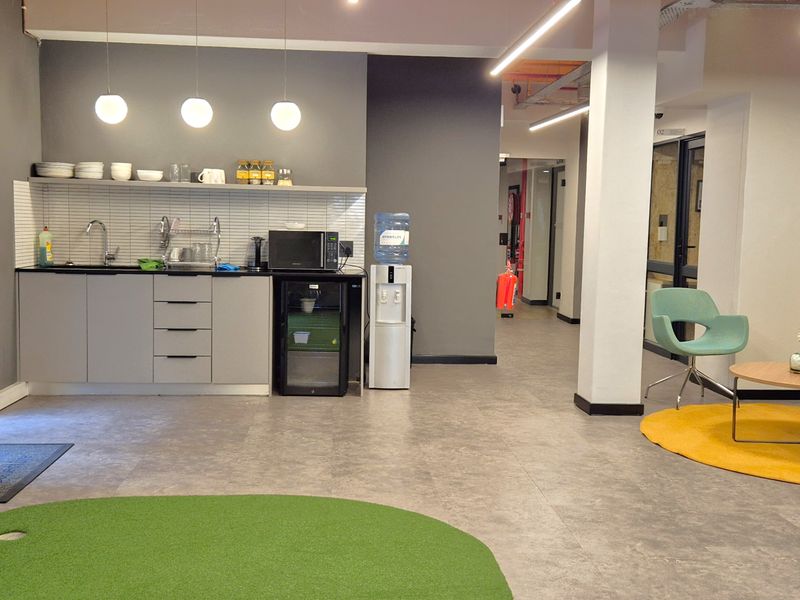 Modern office break area featuring a functional kitchenette with built-in cabinetry, sink, and contemporary lighting, complemented by open-plan seating space.