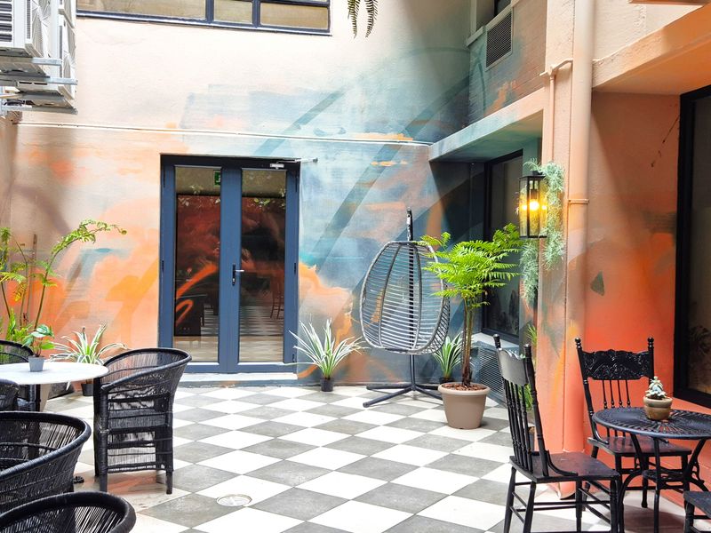 A vibrant, enclosed outdoor patio area featuring checkered tile flooring, decorative wall murals, and integrated wall lighting, providing a unique breakout space.