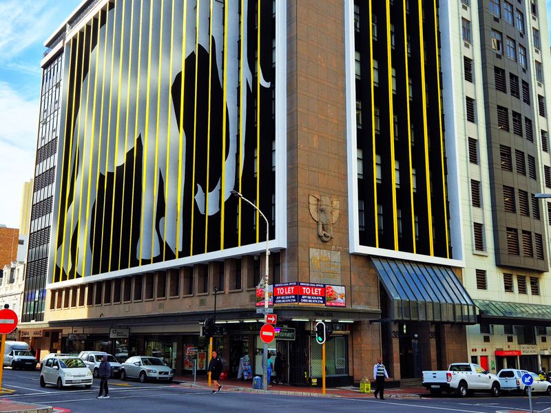 A prominent multi-story commercial office building featuring a distinctive elephant mural facade, street-level retail units, and a busy urban corner location.