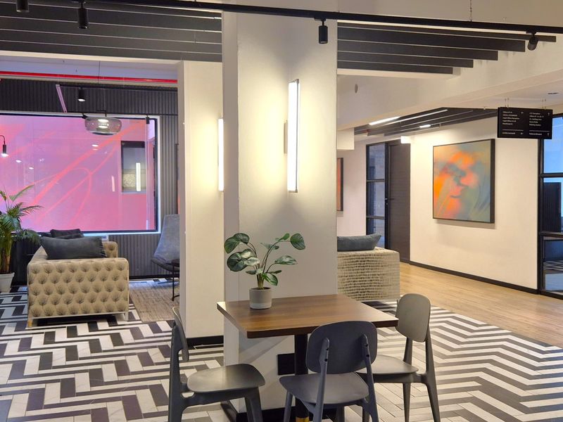 Modern open-plan office breakout area featuring a mix of herringbone tile and laminate flooring, exposed ceiling beams, and contemporary track lighting.