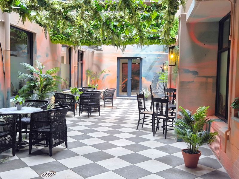 A well-maintained outdoor patio area featuring checkered tile flooring, overhead greenery, and decorative wall finishes, providing a pleasant space for office staff or visitors.