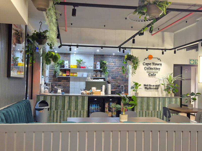Modern open-plan office cafe area featuring a brick accent wall, service counter with integrated refrigeration, and industrial-style exposed ceiling infrastructure.