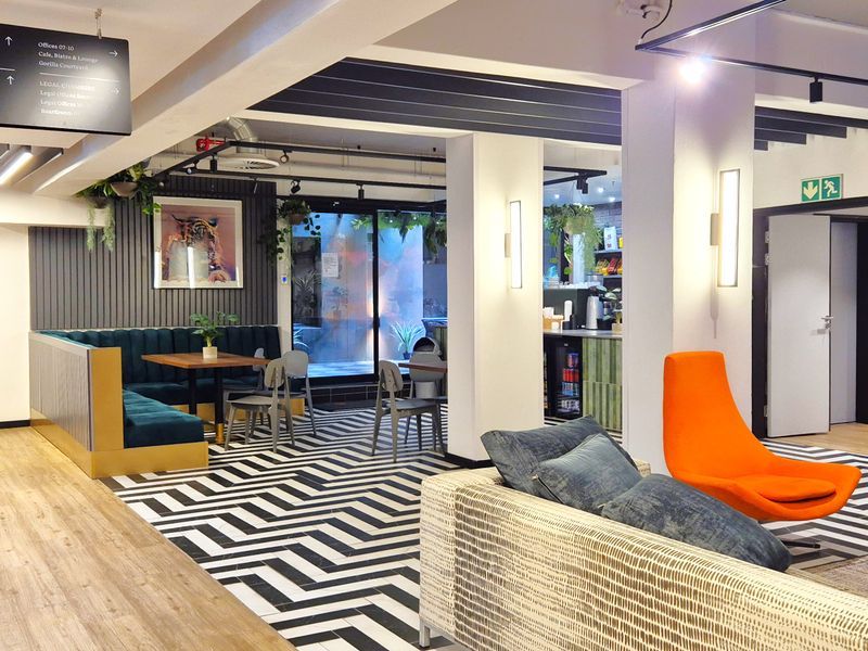 Modern open-plan office breakout area featuring a mix of wood-look flooring, patterned tiling, exposed brick accents, and integrated wayfinding signage.