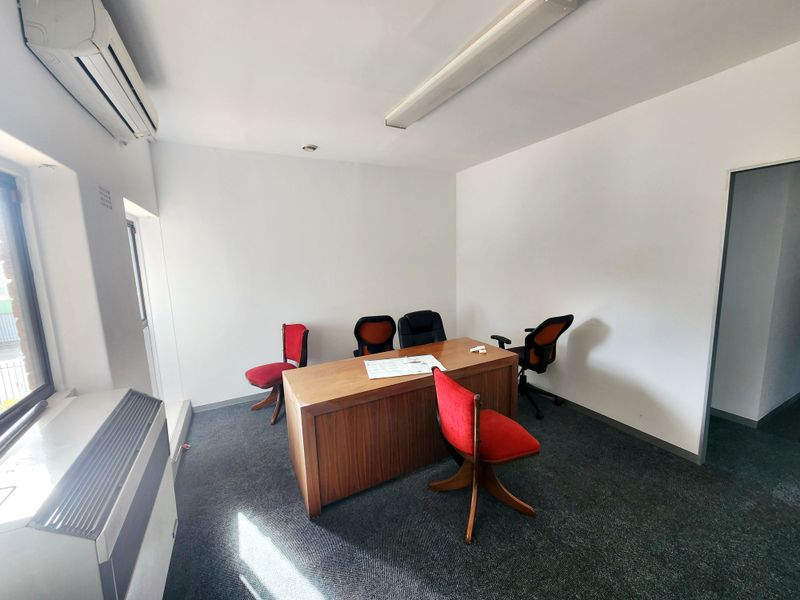 A functional office space featuring carpeted flooring, a wall-mounted air conditioning unit, and overhead fluorescent lighting.