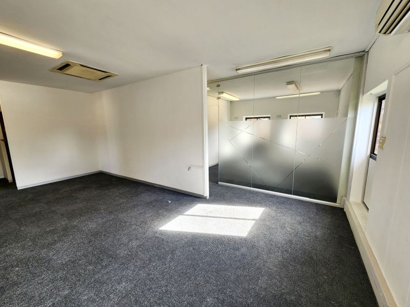 An open-plan office space featuring a glass partition wall, recessed air conditioning, and carpeted flooring, offering a clean and functional professional environment.