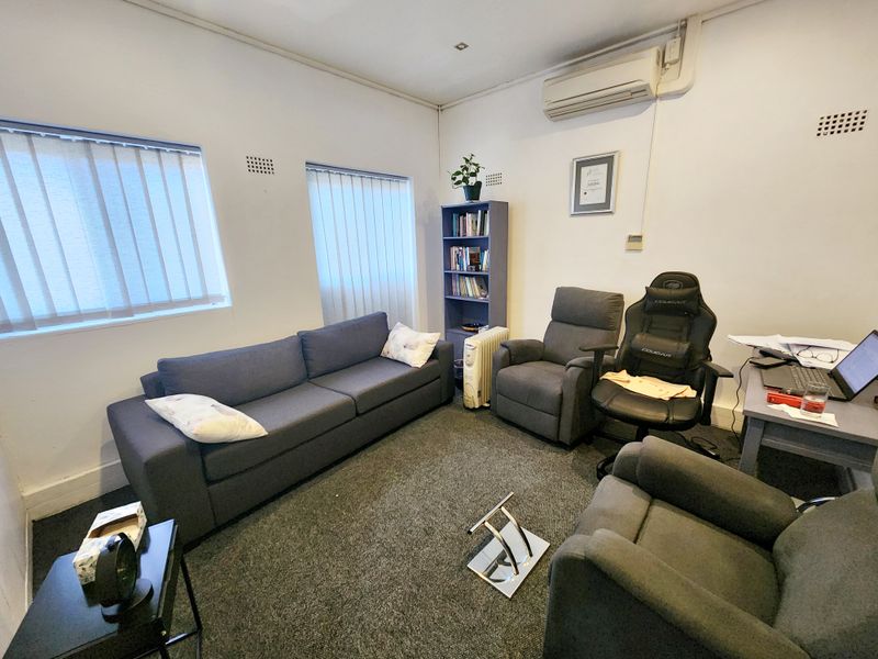 A functional office space featuring carpet flooring, vertical blinds, and a wall-mounted split-system air conditioning unit.