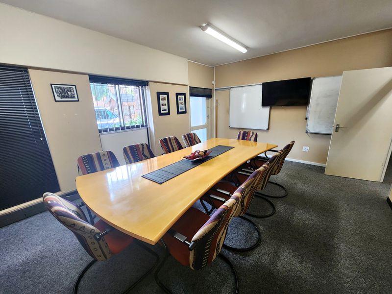 A functional office meeting room featuring carpeted flooring, wall-mounted whiteboards, and security bars on the windows.
