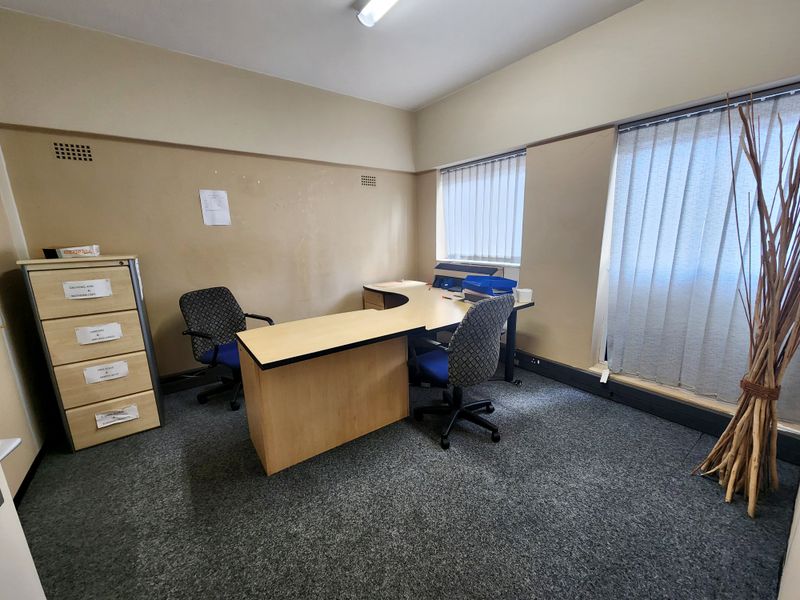 A functional office space featuring carpeted flooring, vertical window blinds, and overhead lighting, suitable for a professional work environment.