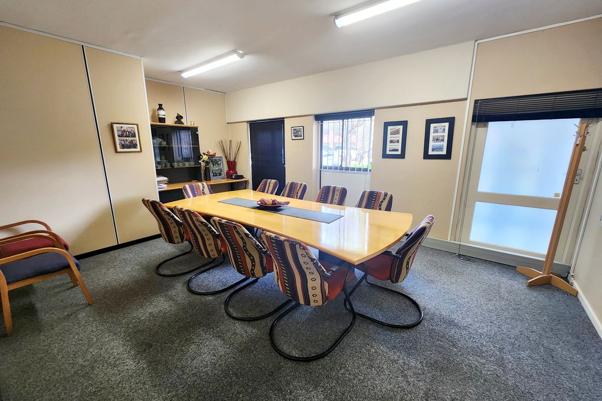 A functional office meeting room featuring carpeted flooring, fluorescent lighting, built-in cabinetry, and a frosted glass entry door.
