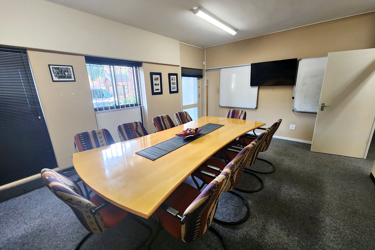 A functional office meeting room featuring carpeted flooring, wall-mounted whiteboards, and security bars on the windows.
