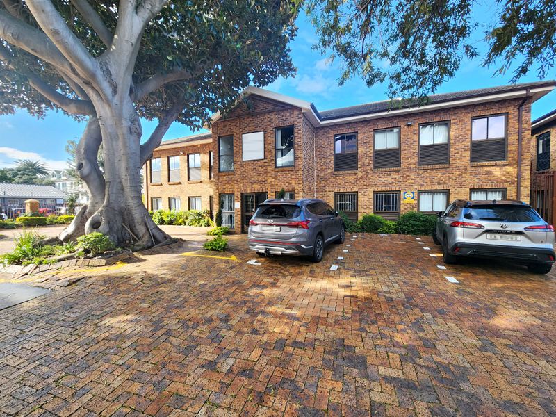 Front exterior view of a two-story face brick office building featuring a paved parking area and mature landscaping.