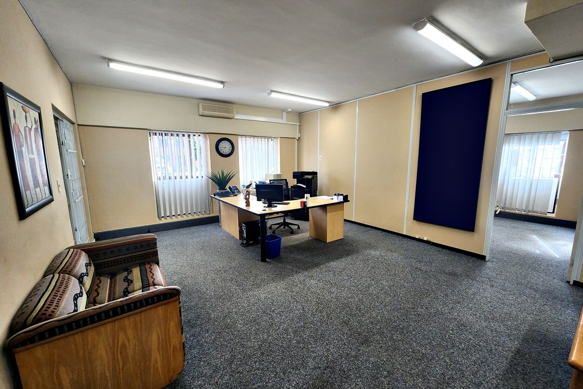 A functional office space featuring carpeted flooring, partitioned walls, vertical blinds, and a wall-mounted air conditioning unit.