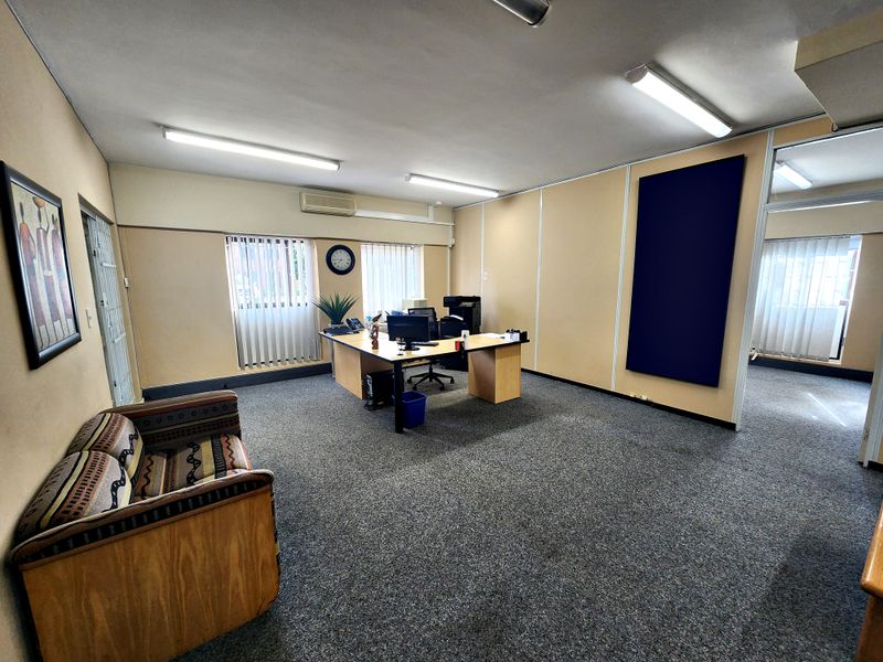A functional office space featuring carpeted flooring, partitioned walls, vertical blinds, and a wall-mounted air conditioning unit.