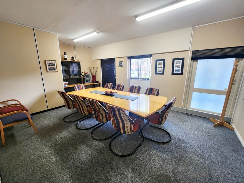A functional office meeting room featuring carpeted flooring, fluorescent lighting, built-in cabinetry, and a frosted glass entry door.