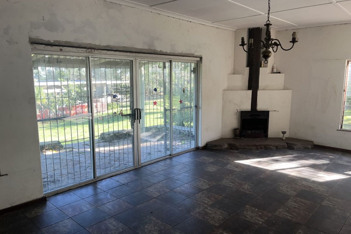 Spacious living area featuring a built-in fireplace, tiled flooring, and large sliding glass doors with security bars, offering direct access to the garden.