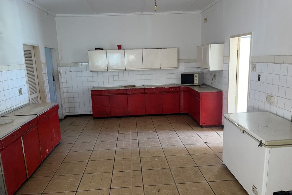A spacious, empty kitchen featuring dated red cabinetry, tiled flooring, and tiled backsplashes, offering a blank canvas for a modern renovation.