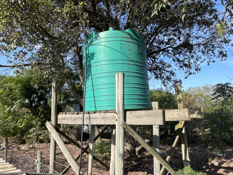 A raised timber platform supporting a green plastic water storage tank located within the garden area.