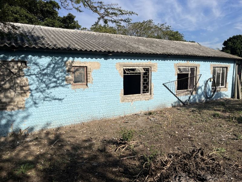 Rear exterior view of a small holding structure showing significant wear to the masonry walls and damaged window frames.