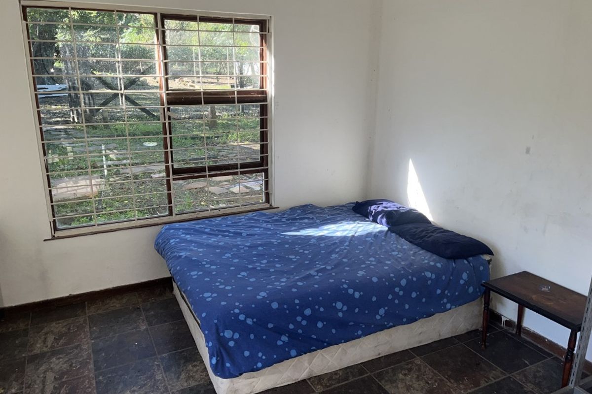 A bedroom featuring tiled flooring and a large window with security bars, offering a view of the garden area.