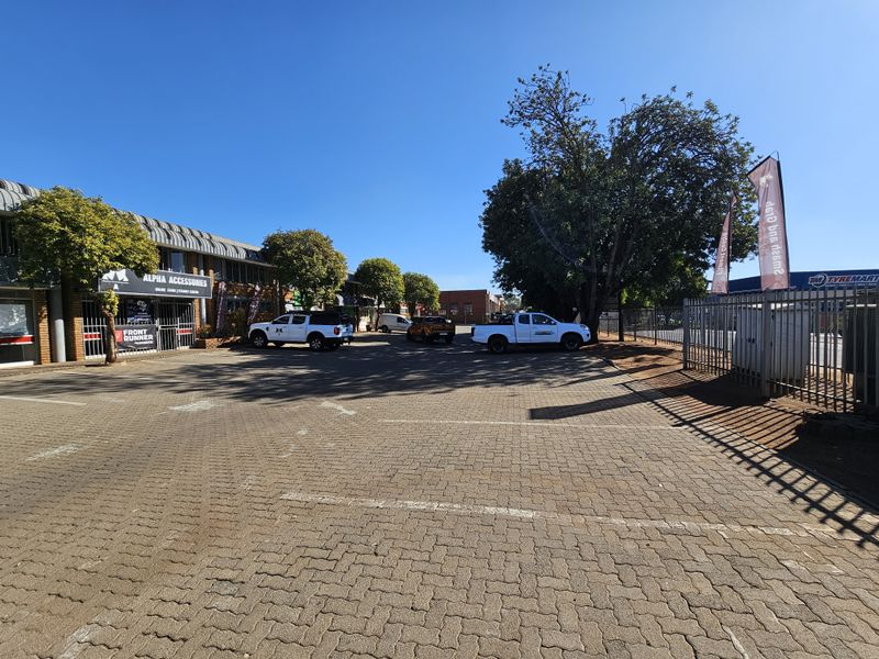 Front exterior view of an industrial commercial complex featuring a paved parking area, brick building facades, and secure perimeter fencing.