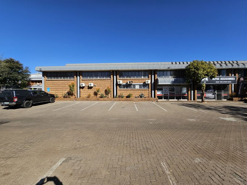 Front elevation of an industrial property featuring a brick facade, metal roofing, and a paved parking area with storefront access.