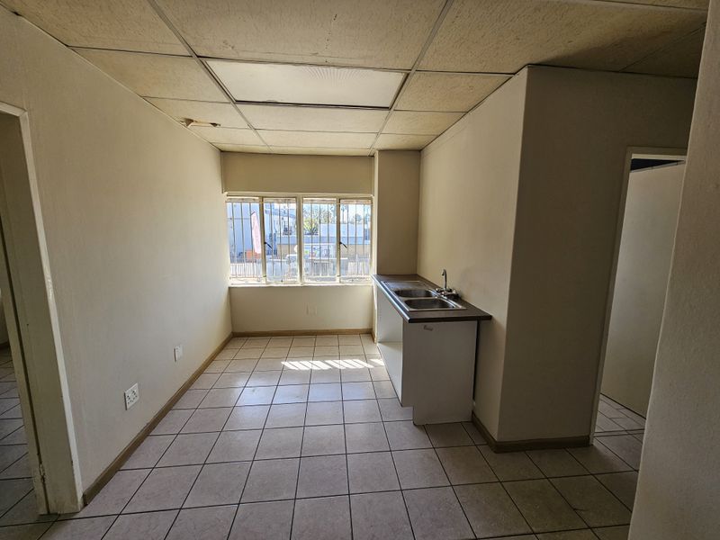 A compact, empty kitchenette featuring tiled flooring, a stainless steel sink, and a drop ceiling, suitable for a small office or industrial utility space.
