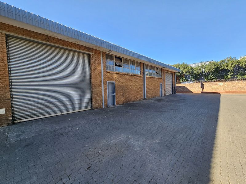 Industrial exterior view featuring a paved yard, brick facade, and multiple roller shutter doors for vehicle access.