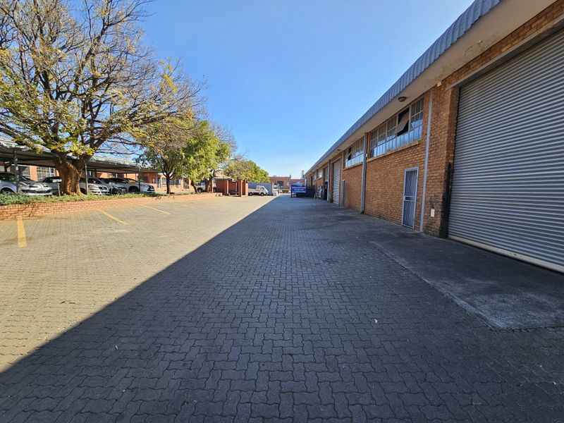 Industrial exterior view featuring a paved driveway, brick facade, and multiple roller shutter doors with adjacent covered parking bays.
