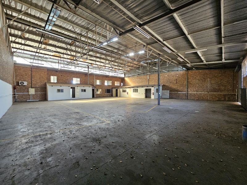 Spacious industrial warehouse featuring exposed brick walls, high steel truss ceilings, concrete flooring, and integrated internal office partitions.