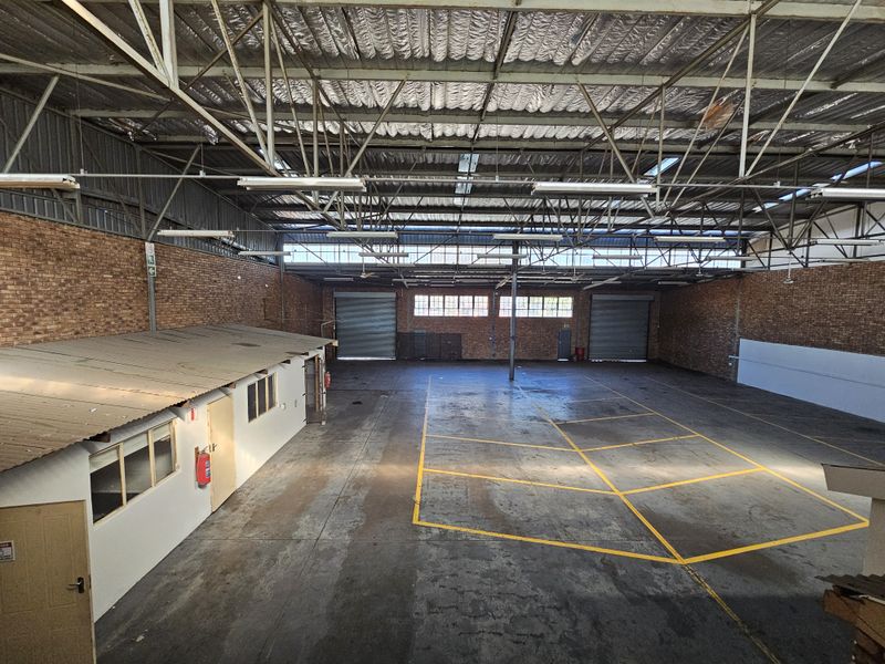 Spacious industrial warehouse featuring high exposed steel trusses, concrete flooring with marked bays, roller shutter access, and an integrated internal office structure.