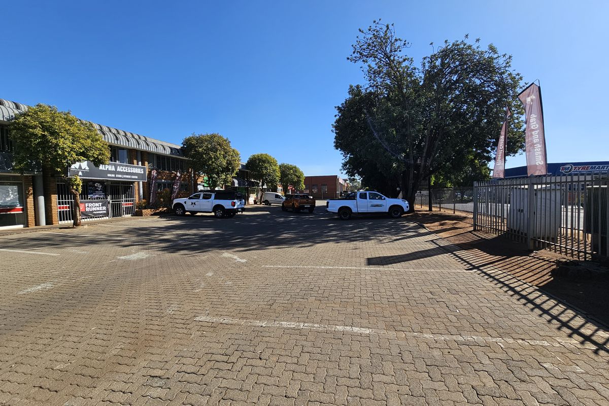 Front exterior view of an industrial commercial complex featuring a paved parking area, brick building facades, and secure perimeter fencing.