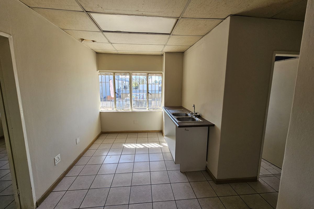 A compact, empty kitchenette featuring tiled flooring, a stainless steel sink, and a drop ceiling, suitable for a small office or industrial utility space.