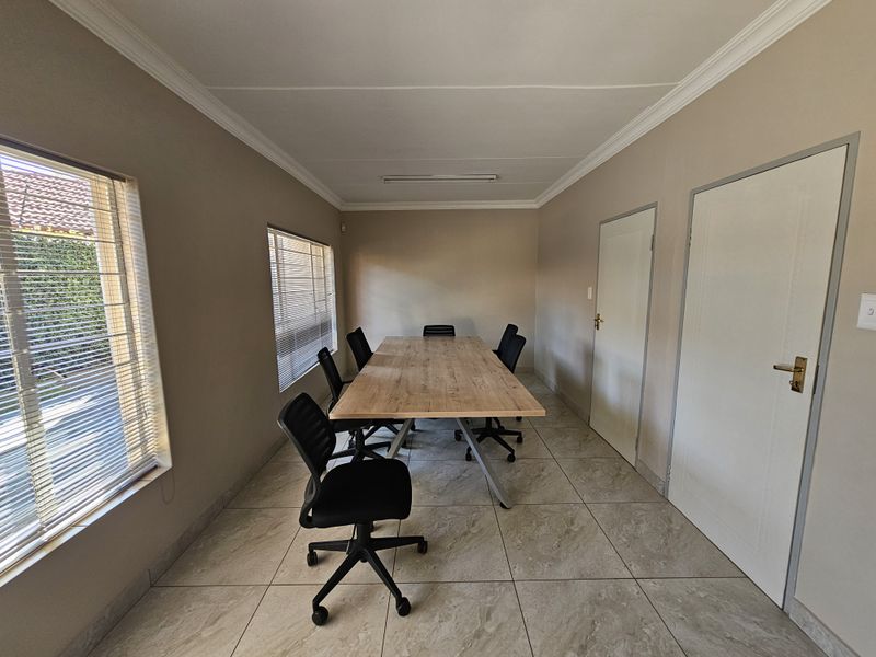 A functional office space featuring tiled flooring, neutral wall tones, and natural light provided by large windows with fitted venetian blinds.